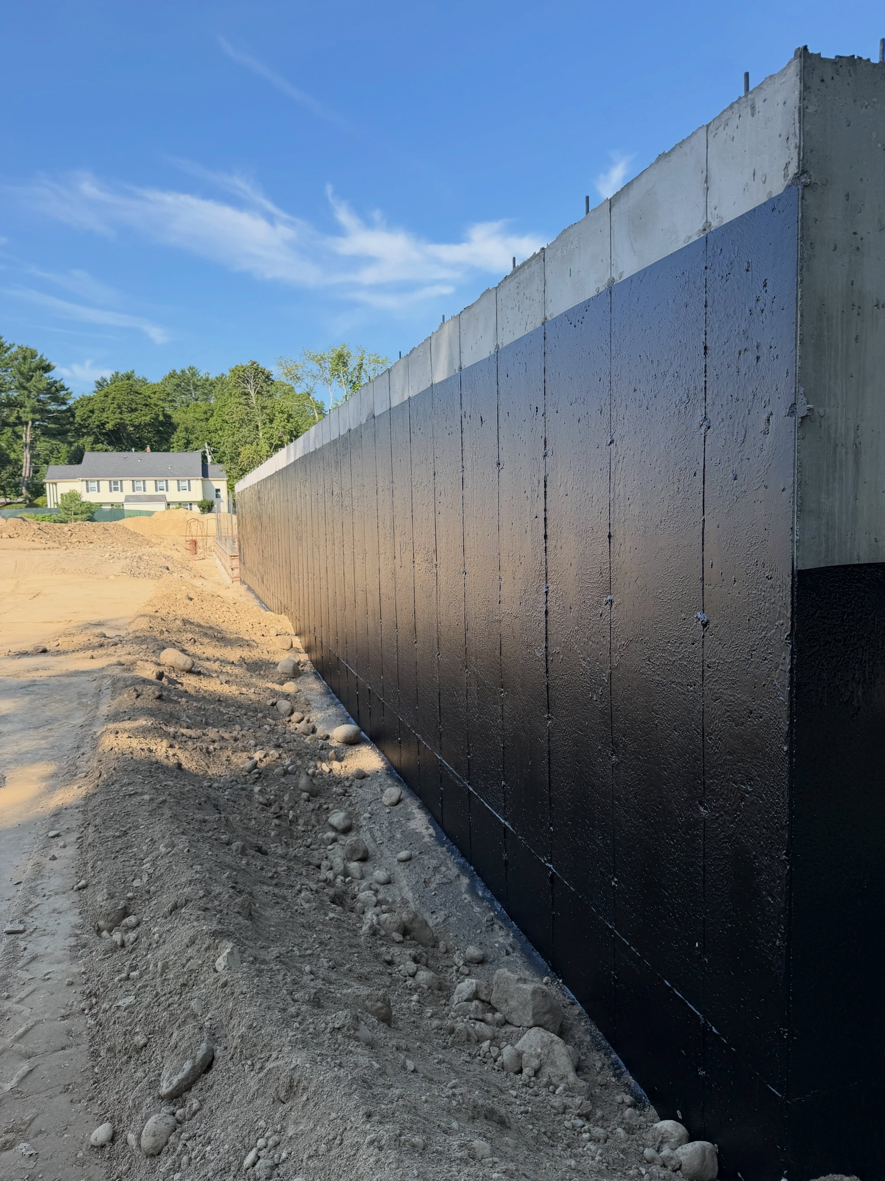 Long foundation wall coated in black waterproofing membrane before backfill