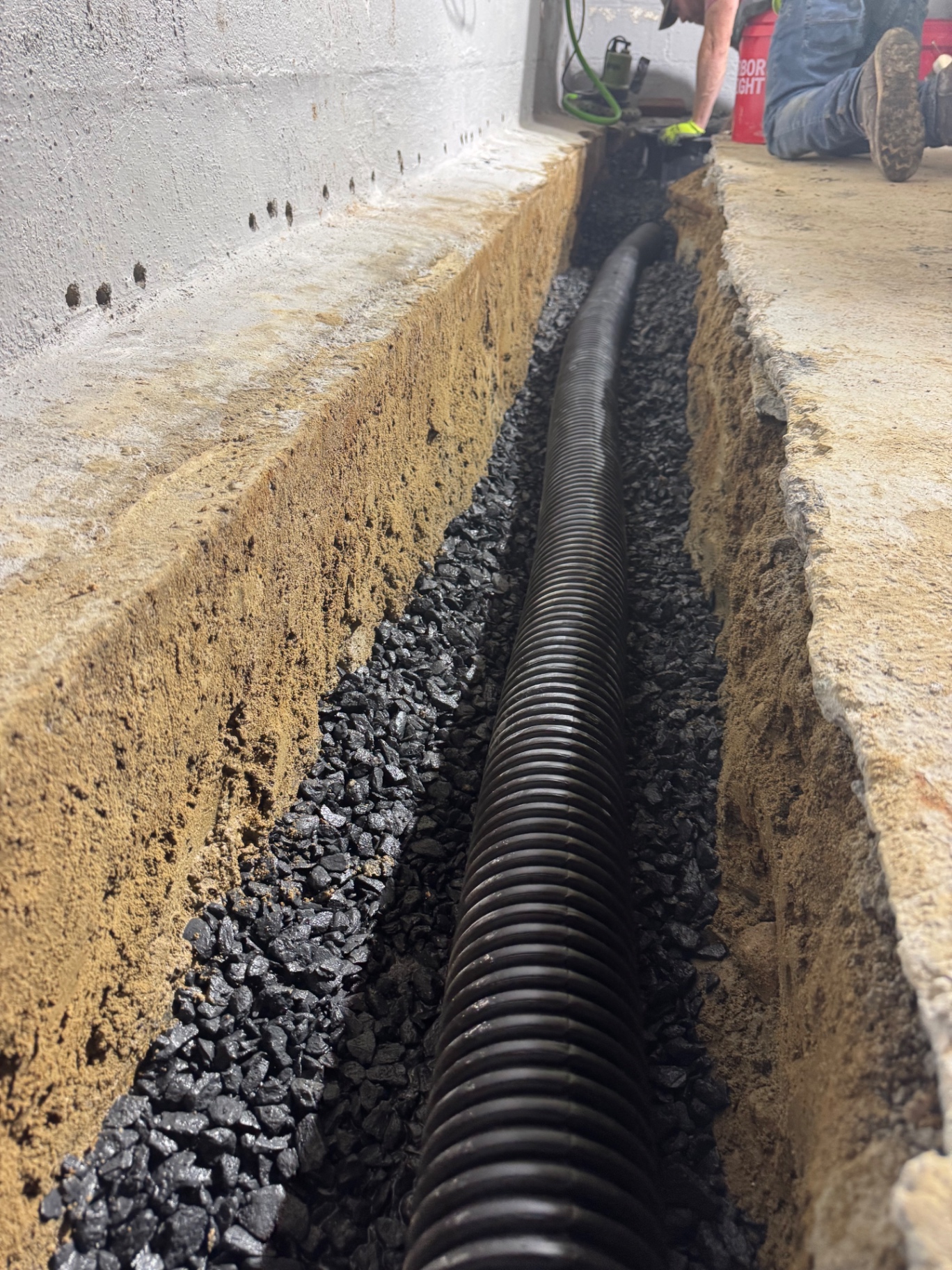 Interior perimeter drain pipe set in stone before the floor is patched